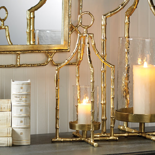 Gold metal candle holders with lit candles, white books, and a gold-framed mirror on a gray surface.