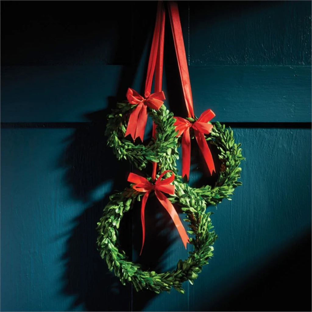 A group of three box wreaths with red bows hanging from a teal door.