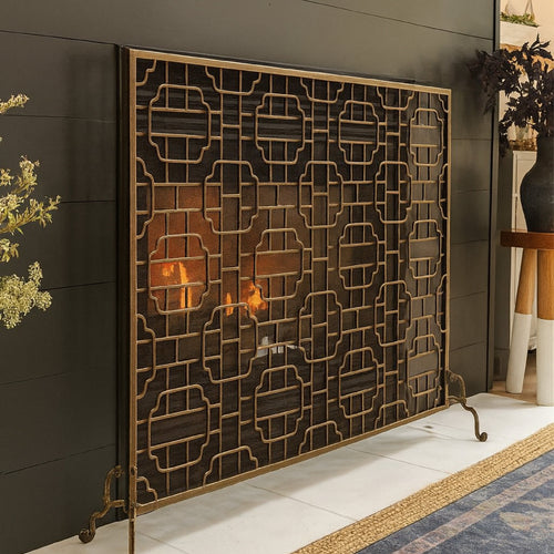 A bronze fireplace screen in front of a black mantel