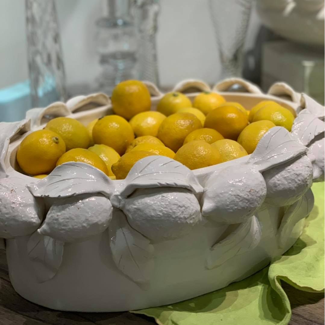 Abigails' Ceramic Lemon Oval Bowl, filled with fresh lemons, sits on a green cloth.