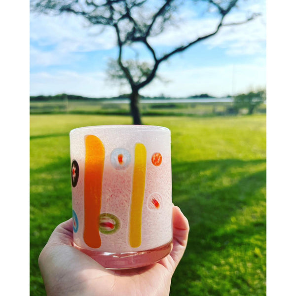 Holding an Abigails White + Multi-Color Cocktail Tumbler set against a sunny backdrop of trees and lush green fields.