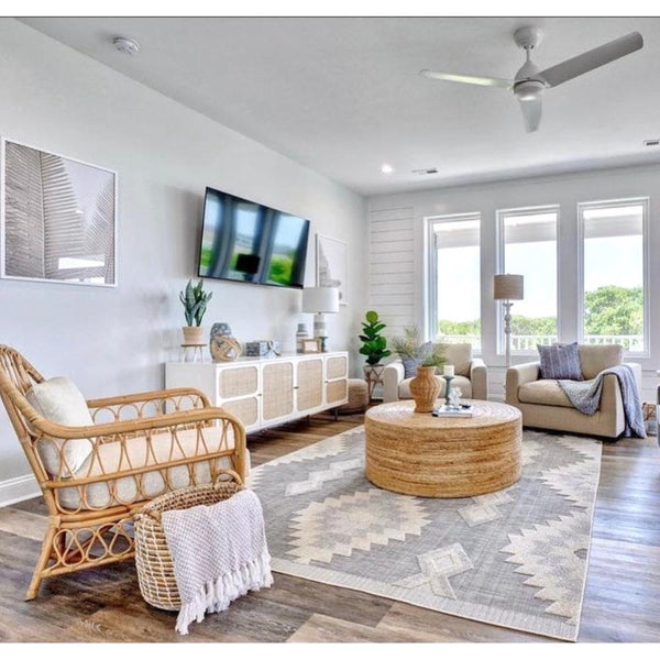 Bright, modern living room with a Kenian Bar Harbor Rattan Club Chair, wall art, plush cream cushion, and patterned rug.