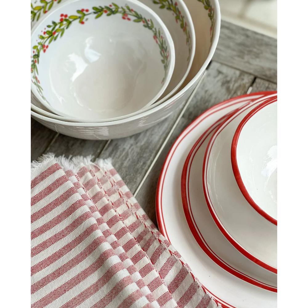 Set of white bowls with red and green patterns on a wooden surface with a striped cloth.