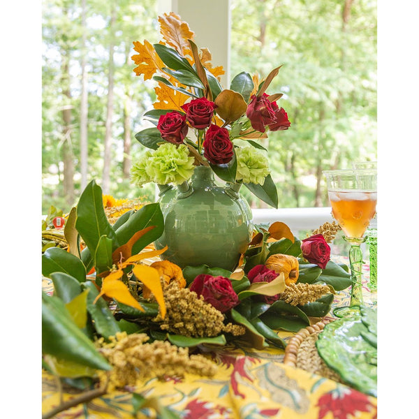 Decorative floral arrangement with a green vase on a table outdoors.