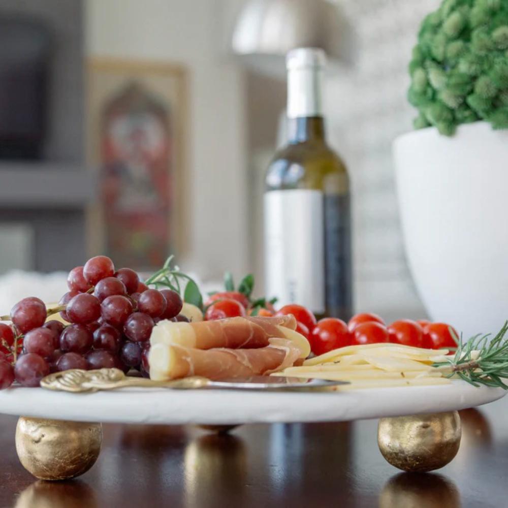Platter of assorted cheeses, fruits, and tomatoes with a bottle of white wine in the background.