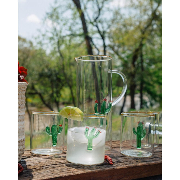 Clear pitcher and glasses with cactus designs on a wooden surface outdoors.