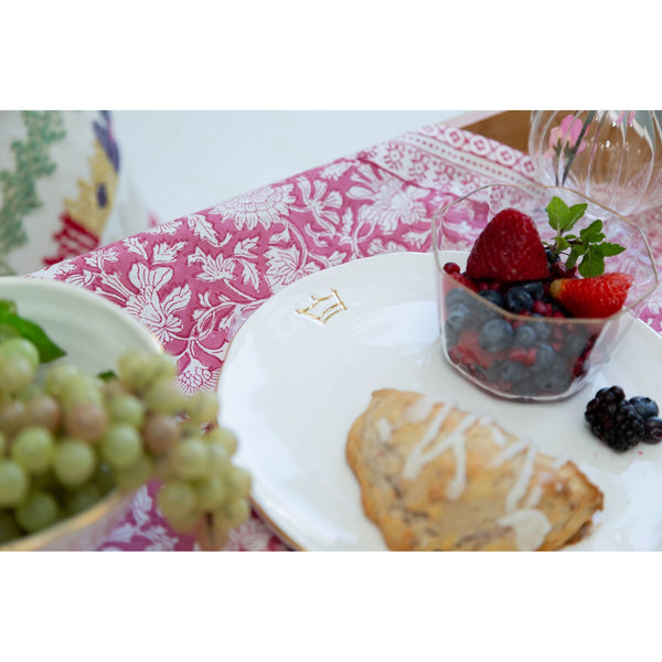 Dessert plate with pastries, berries, and a glass of water on a patterned tablecloth.