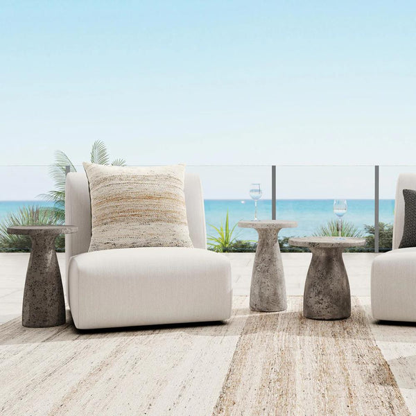 Modern outdoor seating area with white chairs and a Classic Home Collins Concrete Accent Table, ocean view in background.