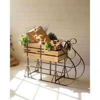 Wooden sleigh with Christmas decorations and presents on a white wooden floor.