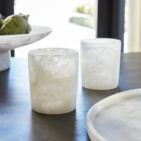 Two Resin White Tumbler Glasses by Santa Barbara Design Studio sit on a dark table near a matching plate and bowl.