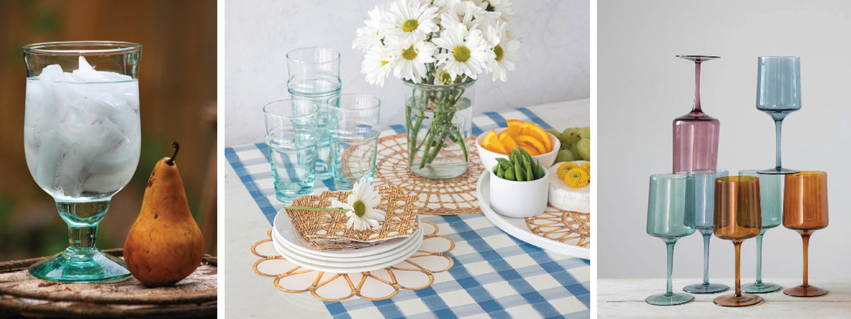 a green glass water goblet, paper placemats or charger in basket print on a table, and a stack of colorful wine glasses