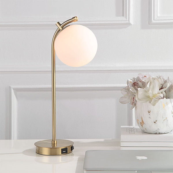 The Uttermost Glass Globe Desk Lamp with USB port sits by a laptop and flowers on the desk.