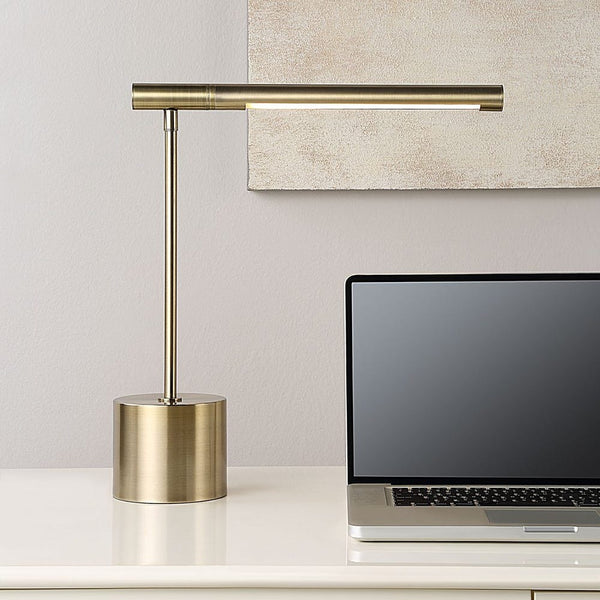 Uttermost Antique Brass Desk Lamp with rotating arm sits beside a laptop on a white desk, canvas art on wall.