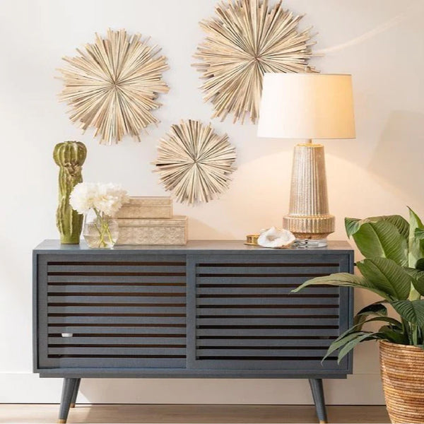 Modern sideboard in a coastal setting featuring Made Goods' Wickham Teak Wall Sculptures (set of 2) as artful wall decor, paired with a lamp, books, cactus, and plant against a light-colored wall and floor.