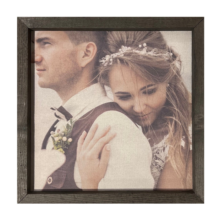 Capture the cherished moment of a couple on their wedding day with Brayden & Brooks' Thin Wooden Frame Custom Photo Panel. The groom, in a white shirt and vest adorned with a boutonniere, gazes away while the bride, her long hair crowned by a delicate headpiece, smiles warmly as she embraces him from behind. This custom photo panel is perfect for adding to your gallery wall, available in various sizes and finishes to complement any decor style.