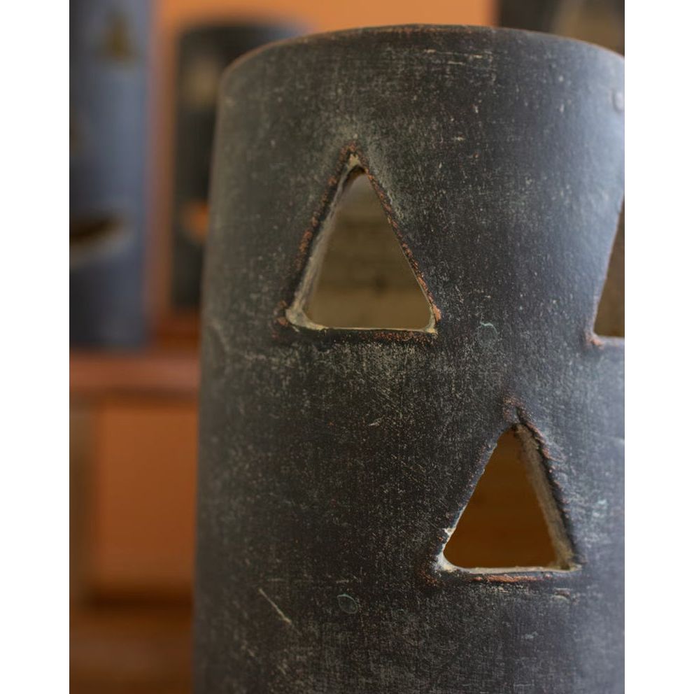 Close-up of a weathered metal cylinder with triangular cutouts, exuding a Halloween charm, set against a blurred background. Featured is one of Kalalou's Black Clay Jack-O-Lanterns from their set of six.