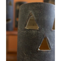 Close-up of a weathered metal cylinder with triangular cutouts, exuding a Halloween charm, set against a blurred background. Featured is one of Kalalou's Black Clay Jack-O-Lanterns from their set of six.