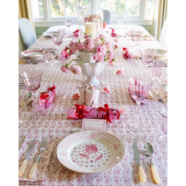 Elegant table setting with a pink floral centerpiece, Abigails Casa Nuno Pink Dinner Plates, glassware, and wrapped gifts.