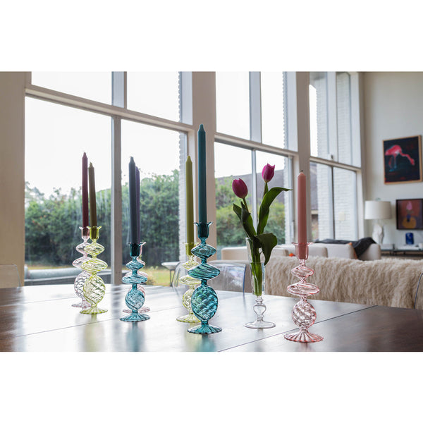 Pink Swirl Glass Candlesticks by Abigails with lit pink taper candles and a vase filled with pink tulips sit elegantly on a wooden table in a well-lit room.