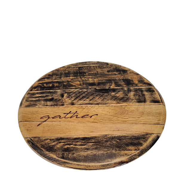 The Bourbon Head Lazy Susan Tray by Sono Inspired is a round wooden board crafted from repurposed bourbon barrel wood, with the word "gather" engraved in a rustic and textured design.