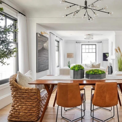 Bright dining room with a wooden table, wicker chairs, potted plant, and large vase with pampas grass on the sideboard.