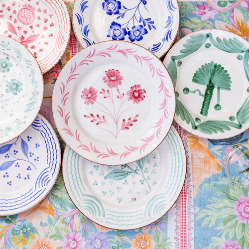 Colorful, vintage ceramic plates with floral patterns arranged on a floral-patterned tablecloth.