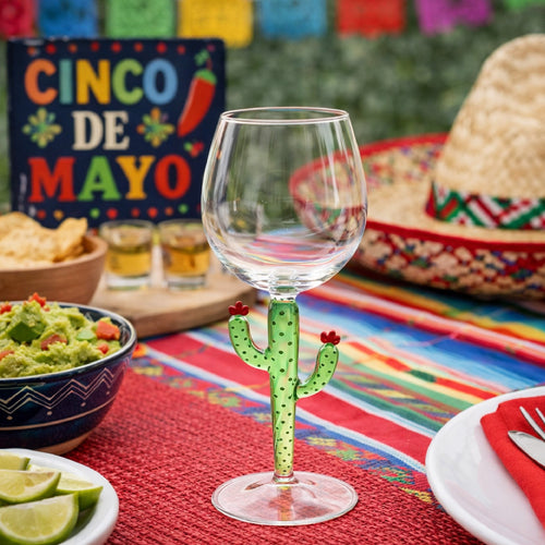 A wine glass with a cactus stem on a colorful table set for Cinco de Mayo with festive decorations.