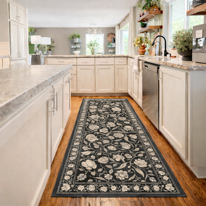 A modern kitchen with light cabinets, wood floors, and a black floral runner rug along the center aisle.