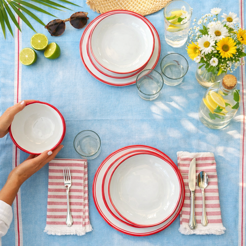Table set for two with striped dishes, drinks, and flowers on a blue cloth; hands holding a bowl.