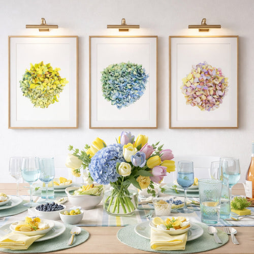 Elegant spring table setting with pastel flowers, blue napkins, and three floral art prints on the wall.
