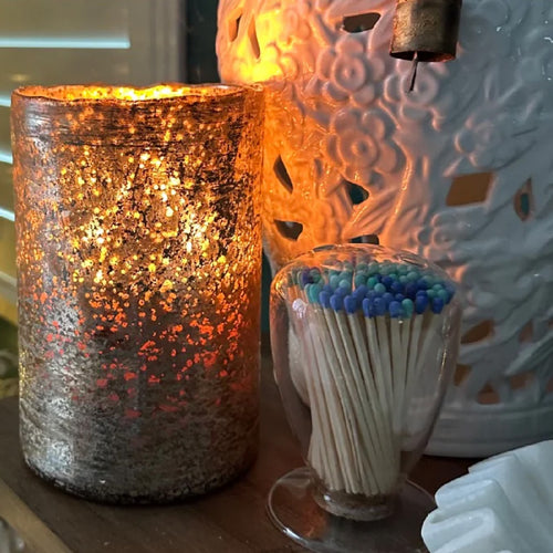 Gold hurricane candle by Himalyan Candles on a table with a match cloche and white jar
