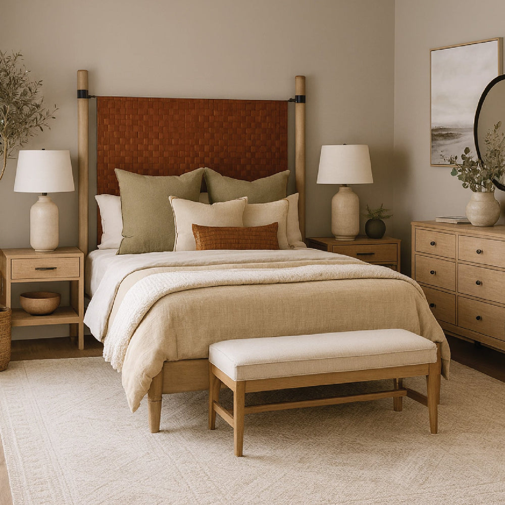 Neutral-toned bedroom with a woven headboard, beige bedding, two nightstands, lamps, and a bench at the foot of the bed.