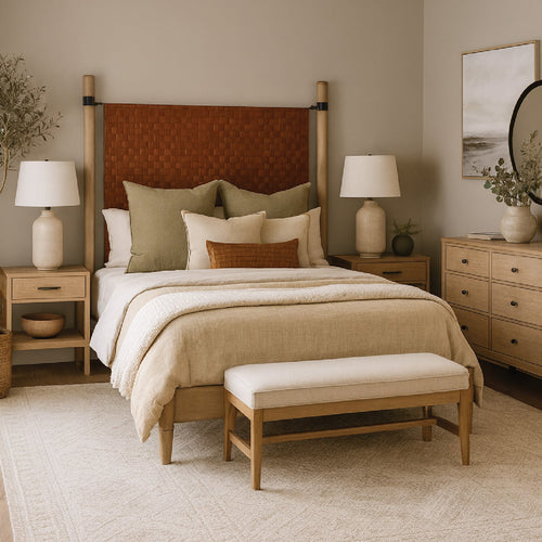 Neutral-toned bedroom with a woven headboard, beige bedding, two nightstands, lamps, and a bench at the foot of the bed.