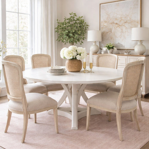 Round white dining table with six beige chairs, floral centerpiece, and neutral decor in a bright room.