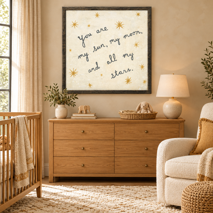 Framed wall art in a nursery featuring the text “you are my sun, my moon, and all my stars” surrounded by gold star icons.