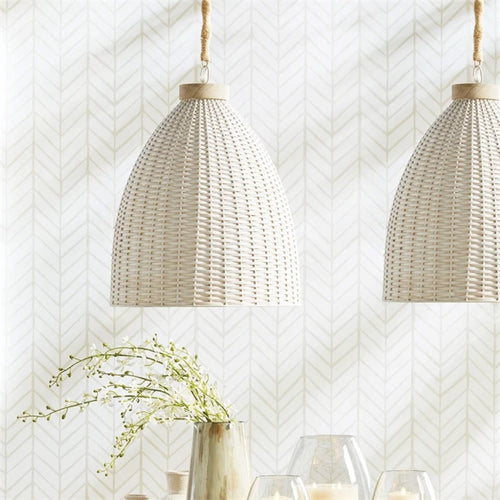 Two woven pendant lights hang above a vase with green branches and glass candle holders on a table.