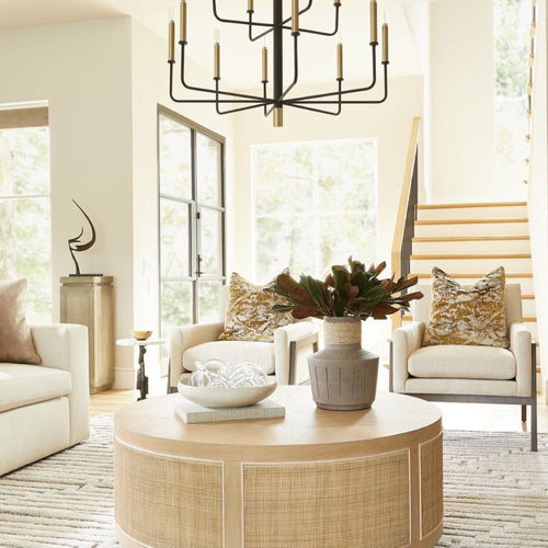 Bright, modern living room with neutral furniture, patterned pillows, a round table, and a large chandelier.