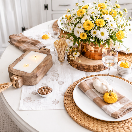 Gold hurricane candle by Himalyan Candles on a table with a match cloche and white jar
