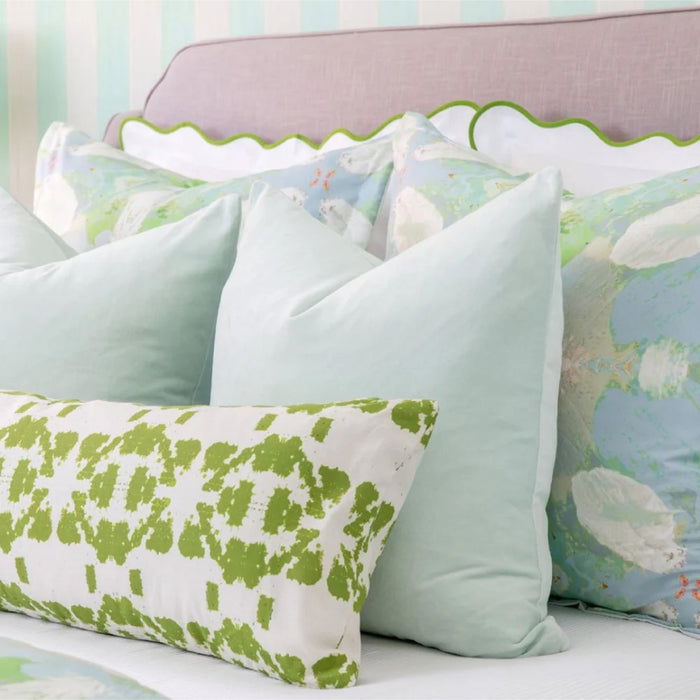 Close-up of a neatly made bed with pastel blue pillows and a green patterned accent pillow.