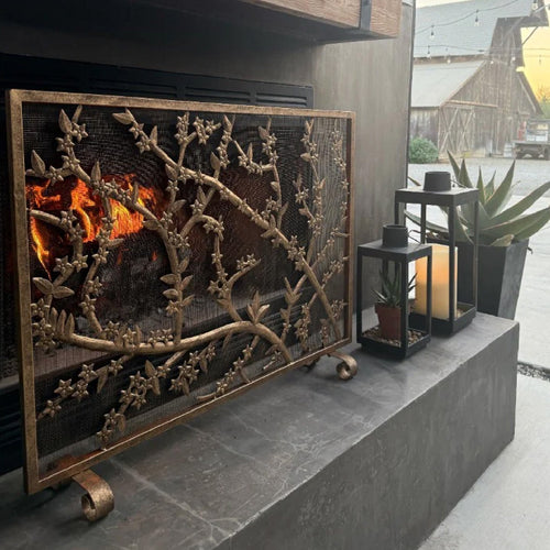 Decorative fireplace screen with floral design, next to lanterns and a potted succulent on a stone hearth.
