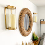 Wall decor with Kalalou glass + antique brass candle wall sconces and a wall-mounted wicker mirror, mini trees on table.