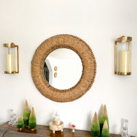 Round mirror, Kalalou brass sconces, and decorative trees on a table.