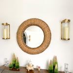 Round mirror, Kalalou brass sconces, and decorative trees on a table.