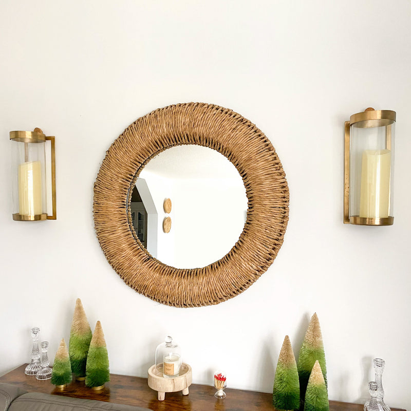 Round mirror, Kalalou brass sconces, and decorative trees on a table.