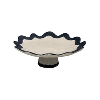 Ceramic footed dish with scalloped edge and navy rim on a white background