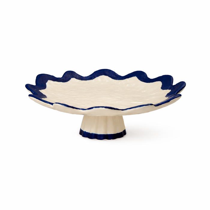 Ceramic footed dish with scalloped edge and navy rim on a white background