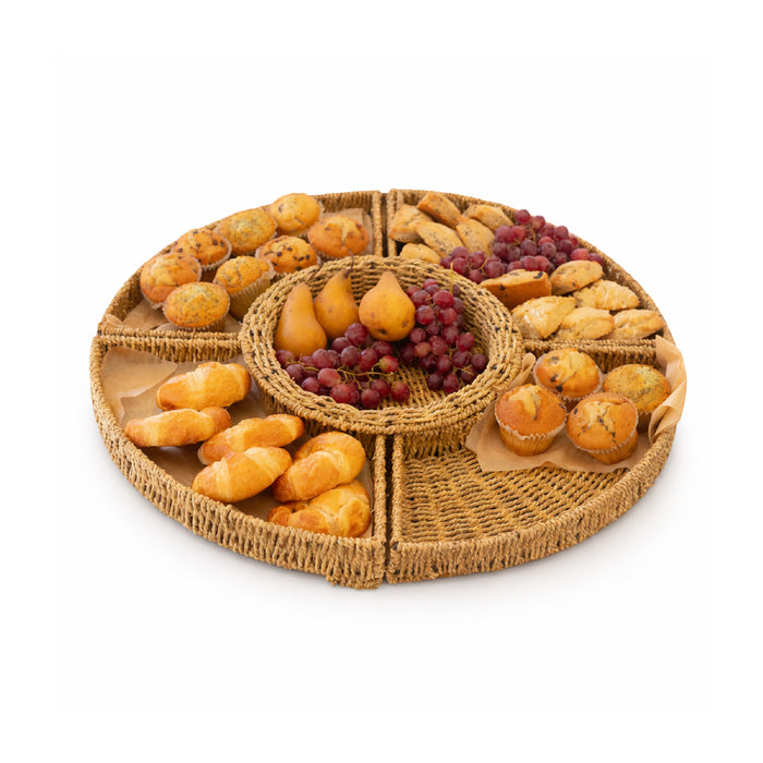 Round wicker charcuterie board with assorted fruits and pastries on a white background