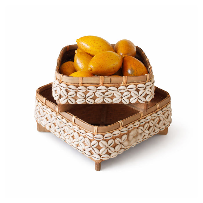 Stack of woven baskets with shell patterns containing yellow fruits on a white background