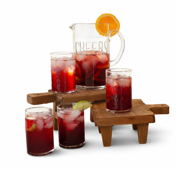 Pitcher and glasses of red iced tea on a wooden stand with 'Cheers' text.