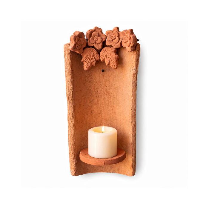 Terra cotta wall-mounted candle holder with floral designs on a white background
